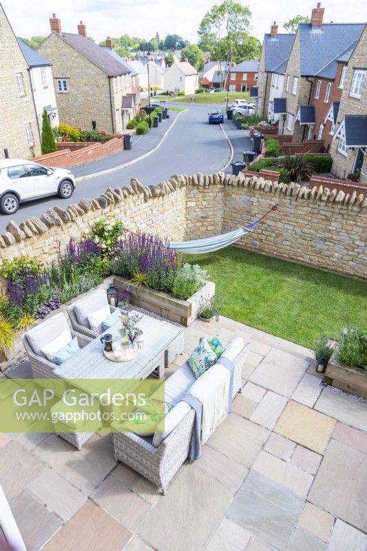 Overview of garden with sofa and chairs, patio, lawn and raised beds