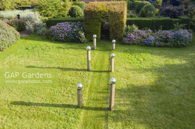 Meadow that has been cut with avenue of columns of wood capped with stainless steel globes and backed by border of Hydrangeas and a clipped tunnel of Hornbeam. September. Image taken with drone. 