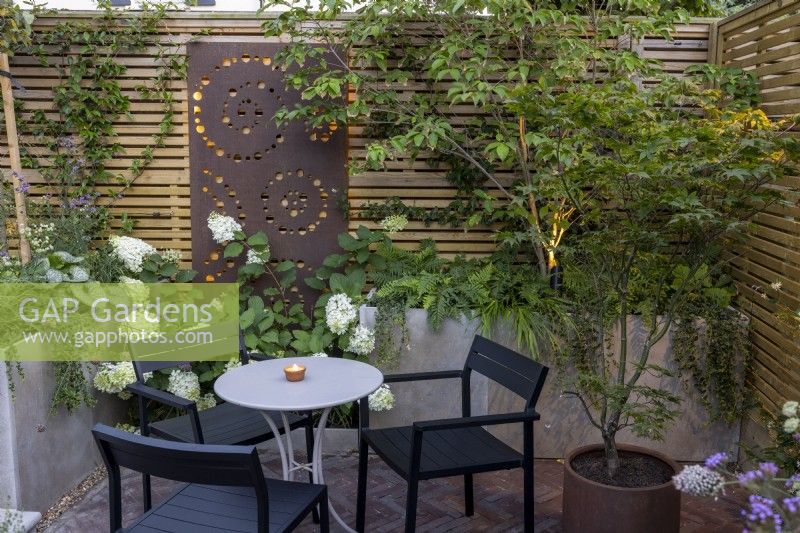 Sitting area at dusk with raised beds and contemporary wood boundary fence with metal screen and lighting