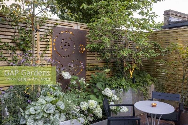 Courtyard garden at dusk with raised beds and contemporary wood boundary fence with metal screen and lighting