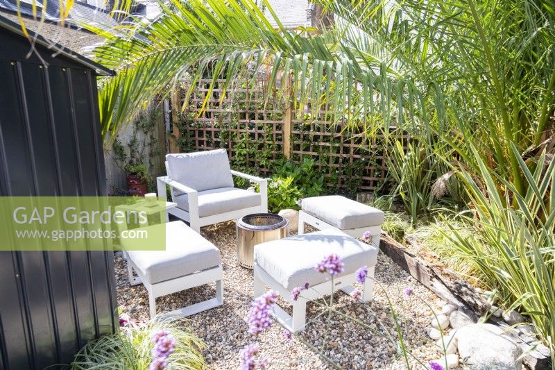 Seating area with firepit in the centre at the end of the garden with large palm tree overhanging