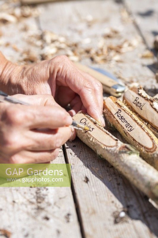 Woman writing herb names on the carved wooden plant lables