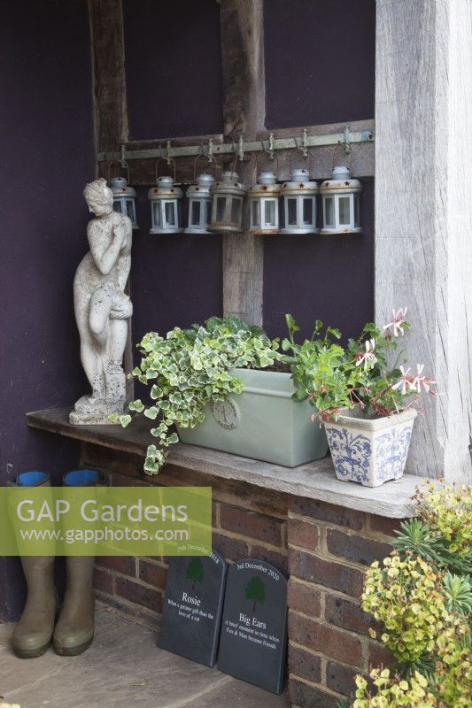 Front porch with wellington boots, candle lamps, a Greek Goddess statue, pet remembrance slate plaques and planted pots. 