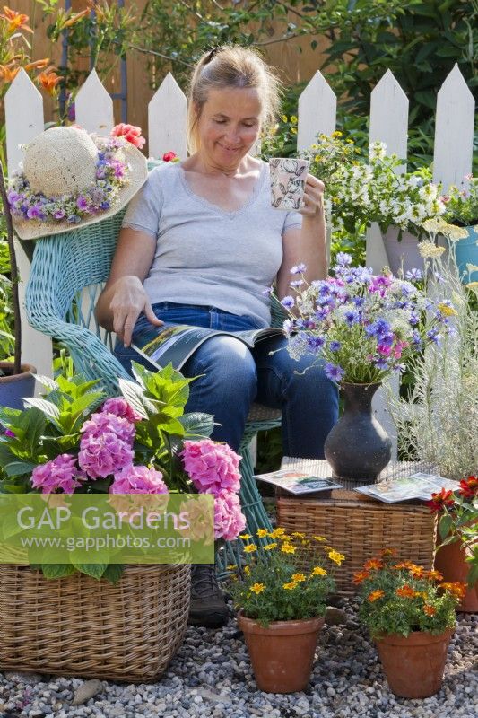 Woman relaxing on gravel terrace with container grown hydrangea and  zinnia.