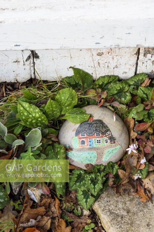 A pebble in a garden with a painted image of a cottage
