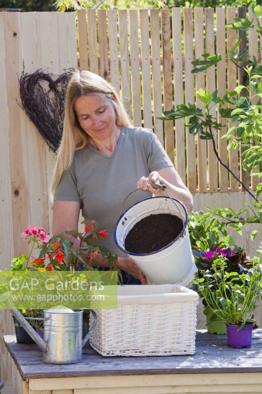 Woman filling wicker container with a mixture of compost and good soil to create good growing condition for plants.
