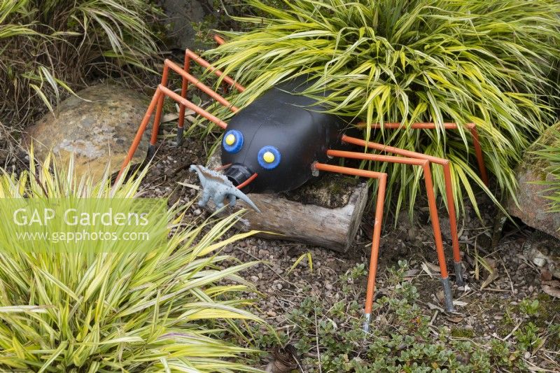 A spider made out of recycled plastic parts hides in foliage. Harbour Lights, Devon NGS garden. July. 
