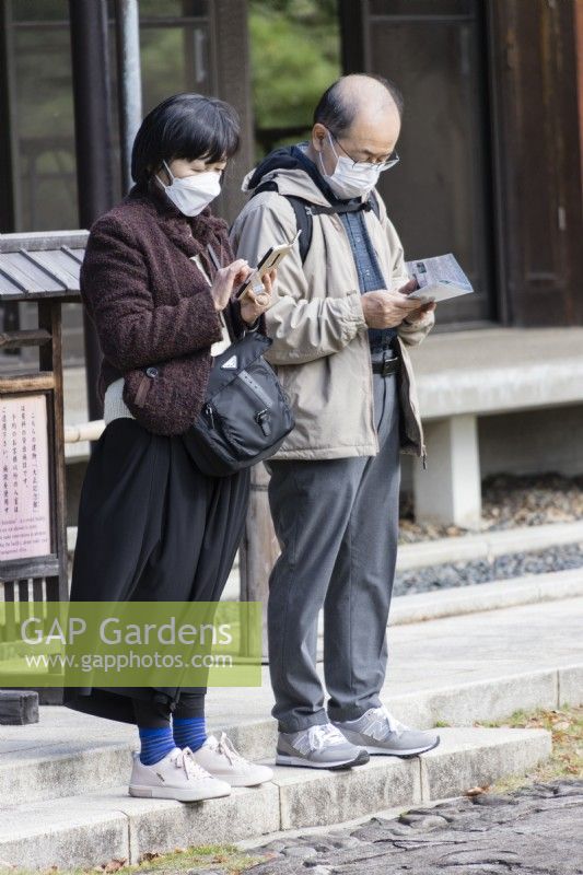 Japanese couple wearing masks looking at information about the garden on a phone and a leaflet. 