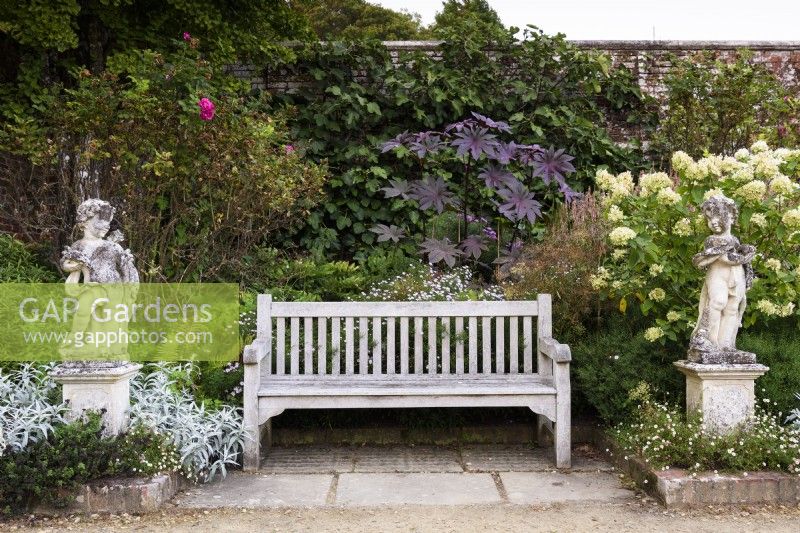 Wooden bench flanked by stone cherubs in the walled garden at Parham House in September