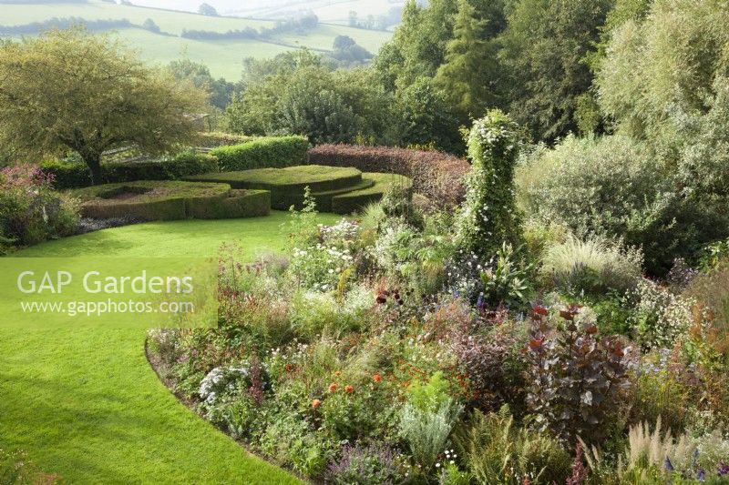 View over lawn and borders to contemporary box and yew topiary with country views beyond.