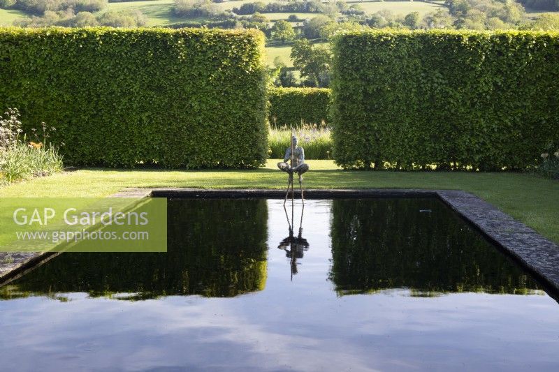 The Bronze Garden - view of reflecting pool with sculpture - a large hedge and countryside in the distance
