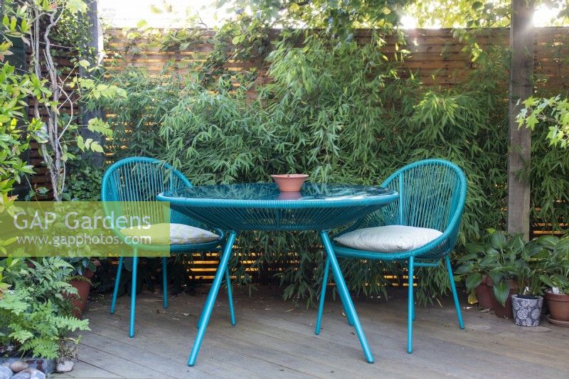 Contemporary style table and chairs at April House, Gloucestershire on a laminate wood deck surrounded by foliage.