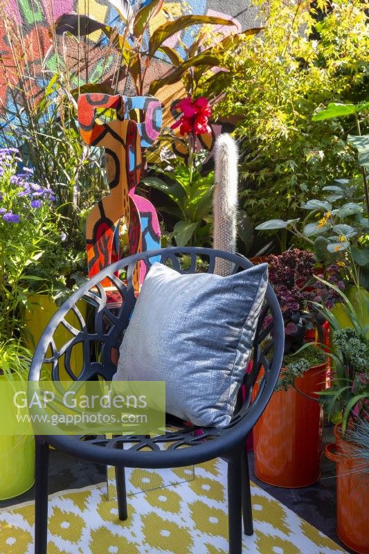 A modern contemporary colourful balcony terrace garden with black chair and cushion - container planting including Miscanthus sinensis 'Dronning Ingrid', Acer, Oreocereus leucotrichus - Old Man of the Andes and Hylotelephium 'Jose Aubergine' - Pop Street Garden RHS Chelsea flower Show September 2021 