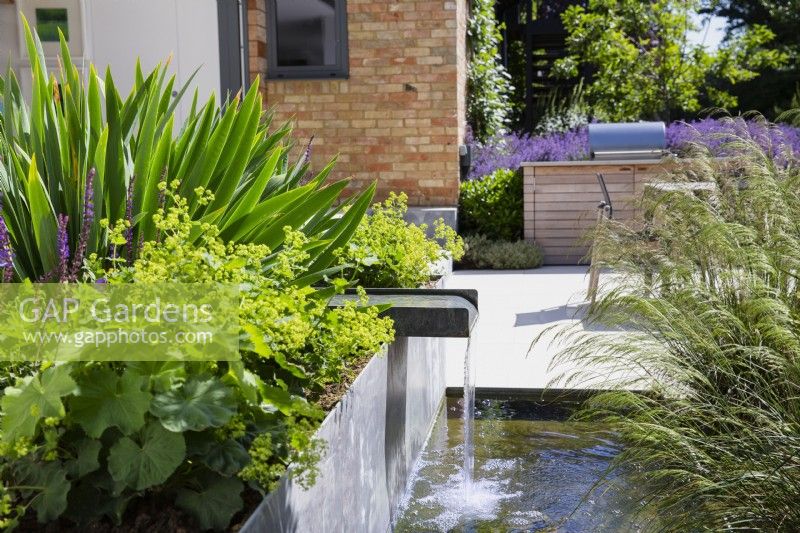 Running water from spout in raised metal flowerbed in modern garden