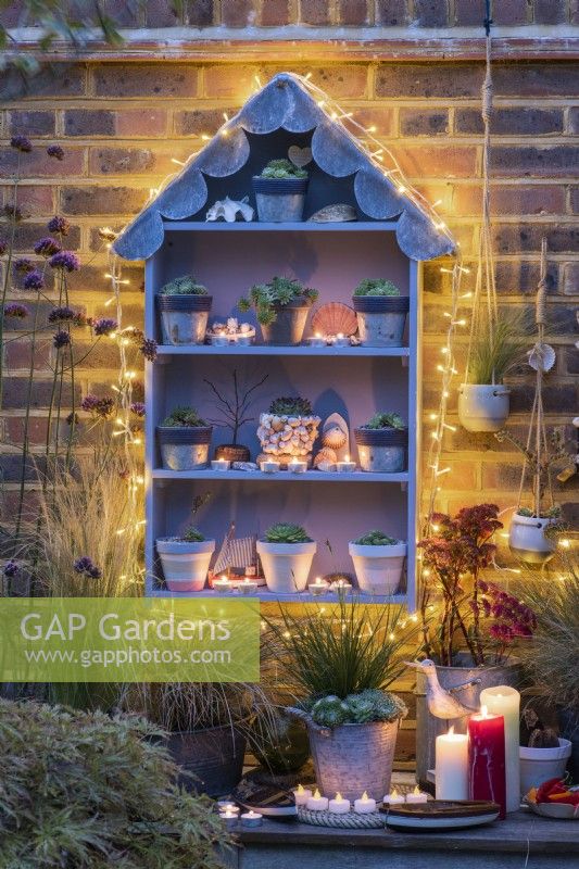 A handbuilt, seaside themed plant theatre with a scalloped lead roof filled with different sempervivum, and lit at night with candles and fairy lights.