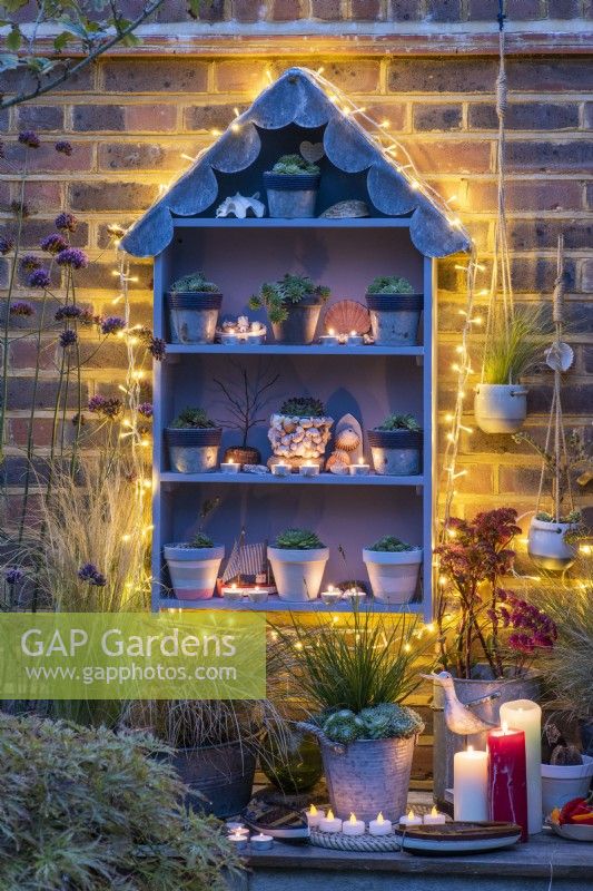 A handbuilt, seaside themed plant theatre with a scalloped lead roof filled with different sempervivum, and lit at night with candles and fairy lights.
