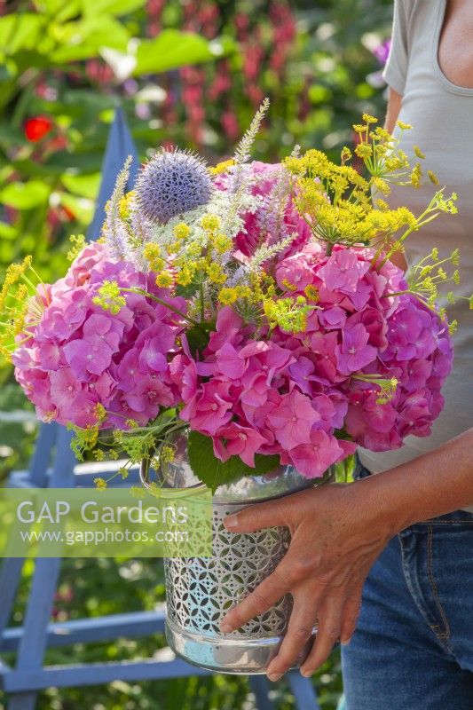 Woman holding vase filled with summer flowers including hydrangea, fennel, veronicastrum and echinops.