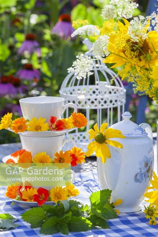 Pot marigolds and nasturtiums on a home-made stand made of teacups and saucers and a teapot with Rudbeckia flower.