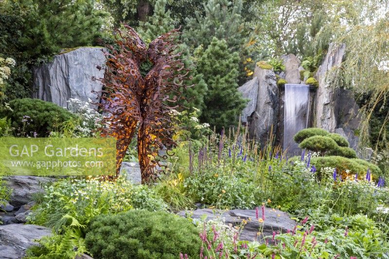 Metal sculpture by Penny Hardy in a rock garden a waterfall and mixed perennial planting of Pines, Willow, Bistorta amplexicaulis 'Atrosanguinea', Veronica longifolia, Chamomile, Achillea millefolium and cloud-pruned Pinus mugo 