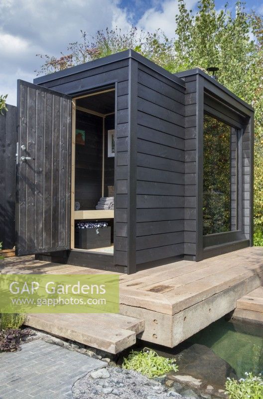 Timber wooden deck over a pool - black painted wood sauna cabin with a living roof planted with wildflowers and herbs
