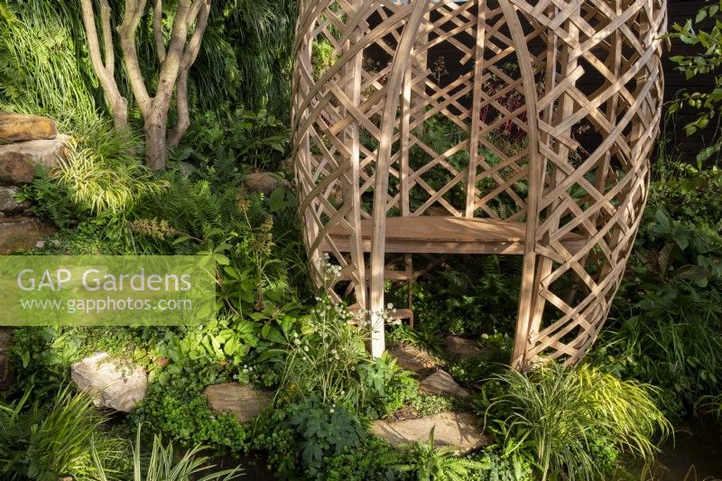 Stepping stones in a damp shady part of the garden leading down to a modern contemporary geodesic laminated lattice-work circular structure made from Moso bamboo - Phyllostachys edulis with a wooden bench seat
