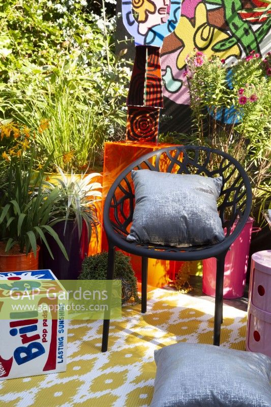 A modern contemporary colourful balcony terrace garden with black chair and cushions - container planting including Symphyotrichum novae-angliae 'Andenken and ornamental grasses