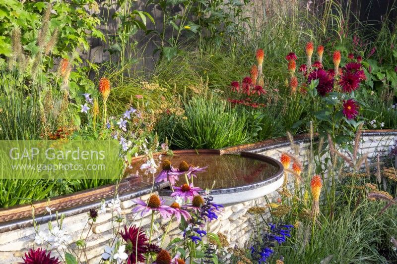 Copper metal rill on a low stone retaining wall with small circular bird bath pool - mixed perennial planting of Echinacea purpurea Magnus and 'Eccentric', Kniphofia 'Papaya Popsicle' - NHS Tribute Garden