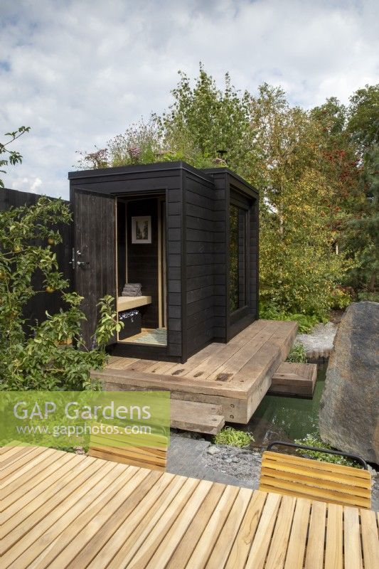 Timber wooden deck over a plunge pool - black painted wood sauna cabin with a living roof planted with wildflowers and herbs - Finnish Soul Garden