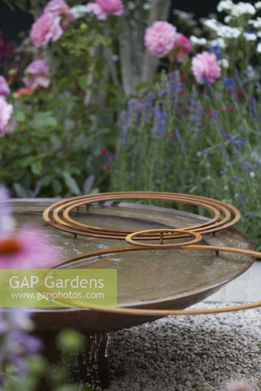 Circular metal water feature with rusty hoops. Summer.