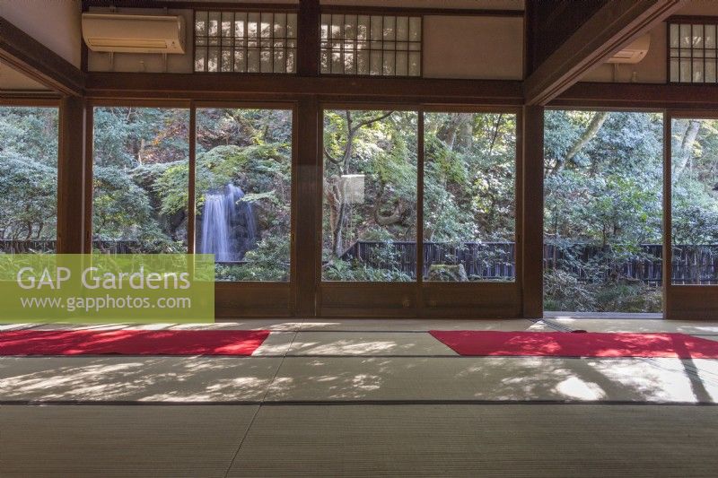 View through room of temple to the garden with a waterfall framed by walls of sliding glass doors. 