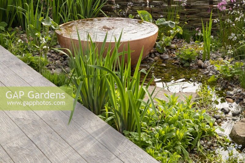 Composite decking board next to a pond with a copper metal container water feature