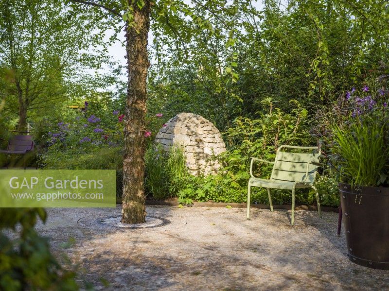 Seating area with green Fernob chair next to Betula nigra and stone cairns at Horatio's Garden, Chelsea Flower Show 2023. Designer: Charlotte Harris and Hugo Bugg, Gold medal winner, Best Show Garden