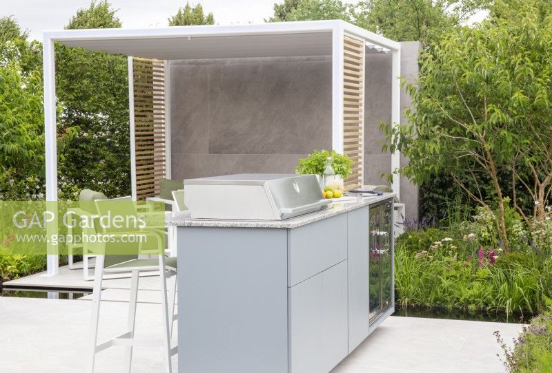 A modern contemporary outdoor kitchen area on a white stone paved patio with a covered pergola