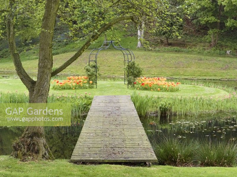 Bridge leading to moated island with metal arch and tulips