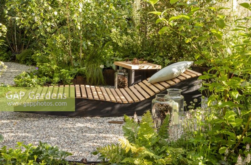 A wooden recliner with cushion, small table in a woodland garden - RHS Hampton Court Palace Show 