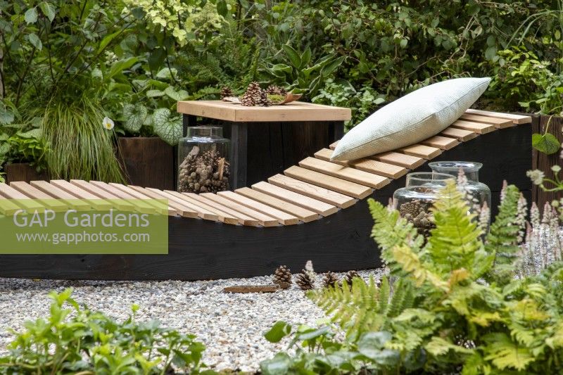 A wooden recliner with cushion, small table in a woodland garden 