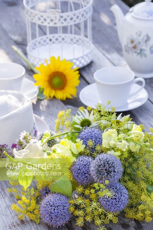 Yellow - blue - white themed bouquet consisting of Echinops, Snapdragon, Fennel, Echinacea, Achillea and Physalis on the table set for tea.