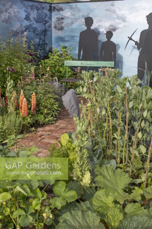 Seating area surrounded by mixed perennials and cut out silhouettes of 'miners in An Imagined Miner's Garden' at RHS Chatsworth Flower Show 2019, June