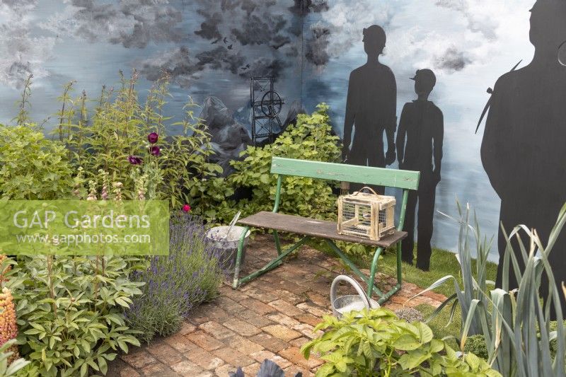 Seating area surrounded by mixed perennials and cut out silhouettes of 'miners in An Imagined Miner's Garden' at RHS Chatsworth Flower Show 2019, June