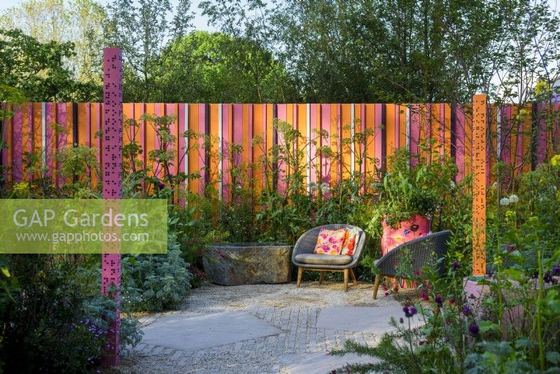 Seating area with two chairs by the wall in orange and pink colours. 
The RHS and Eastern Eye Garden of Unity, Designer: Manoj Malde, Chelsea Flower Show 2023