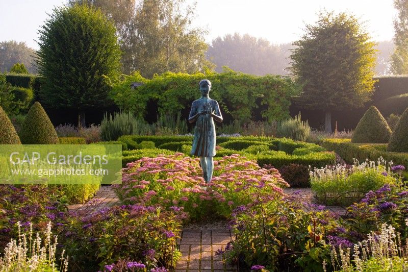 The Lamp of Wisdom statue surrounded by Sedum 'Autumn Joy', Heliotropium arborscens and Box and Yew topiary in the formal garden at Waterperry Gardens