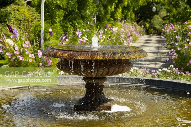 A fountain in a carved stone urn surrounded by summer borders at RHS Garden Wisley.