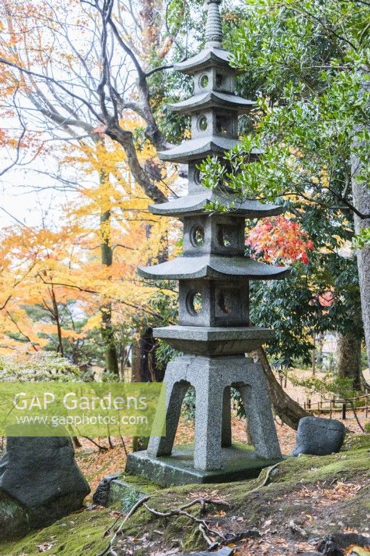 Tall stone pagoda with trees in autumn colour behind. 