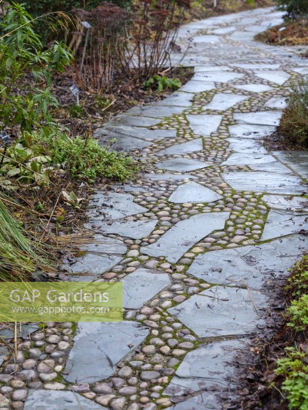 Winding garden path made of river cobblestones and slate, February.