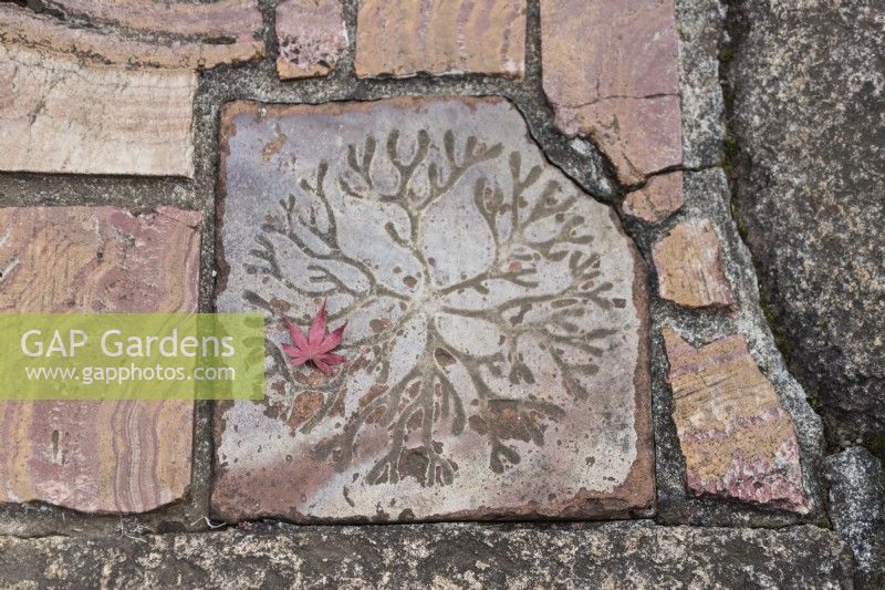 Detail of decorative tile in path with leaf of Acer.