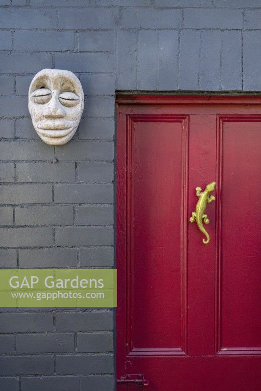Crimson red feature door with a wall mounted tribal mask and a gold lizard door handle.