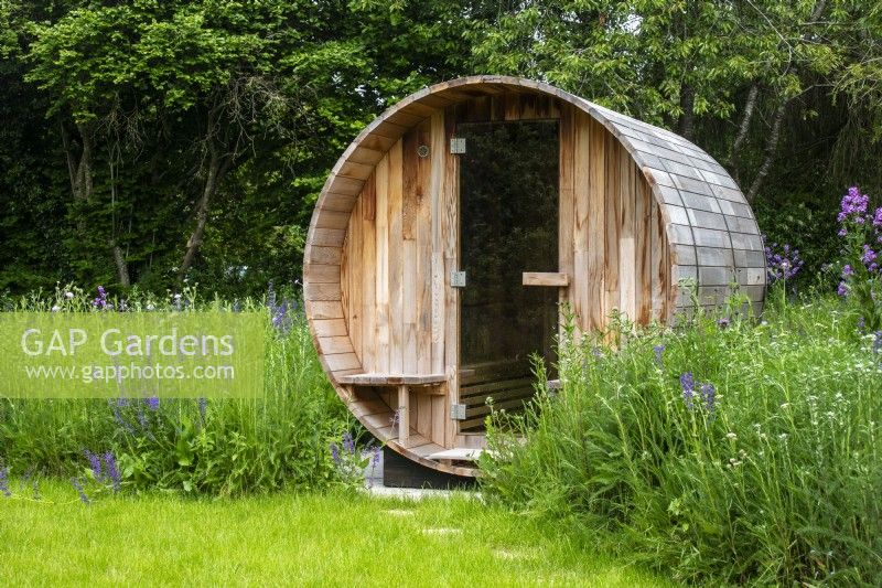 A sauna set into a perennial wildflower meadow with a grass clearing in front.