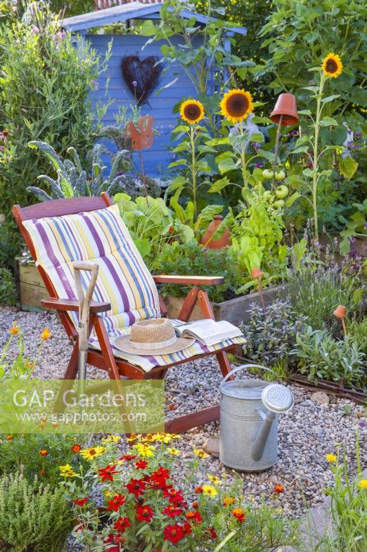 An armchair with a cushion in the kitchen garden with a herb bed, raised beds full of growing vegetables and a variety of flowers to attract beneficial wildlife.