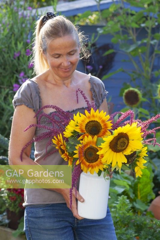 Woman holding bouquet with Sunflowers and Amaranthus caudatus in a milk churn.
