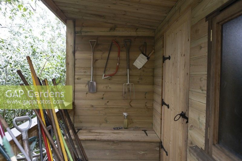 A wooden verandah with saw, fork, spade and paper notebook hung on the back wall. 